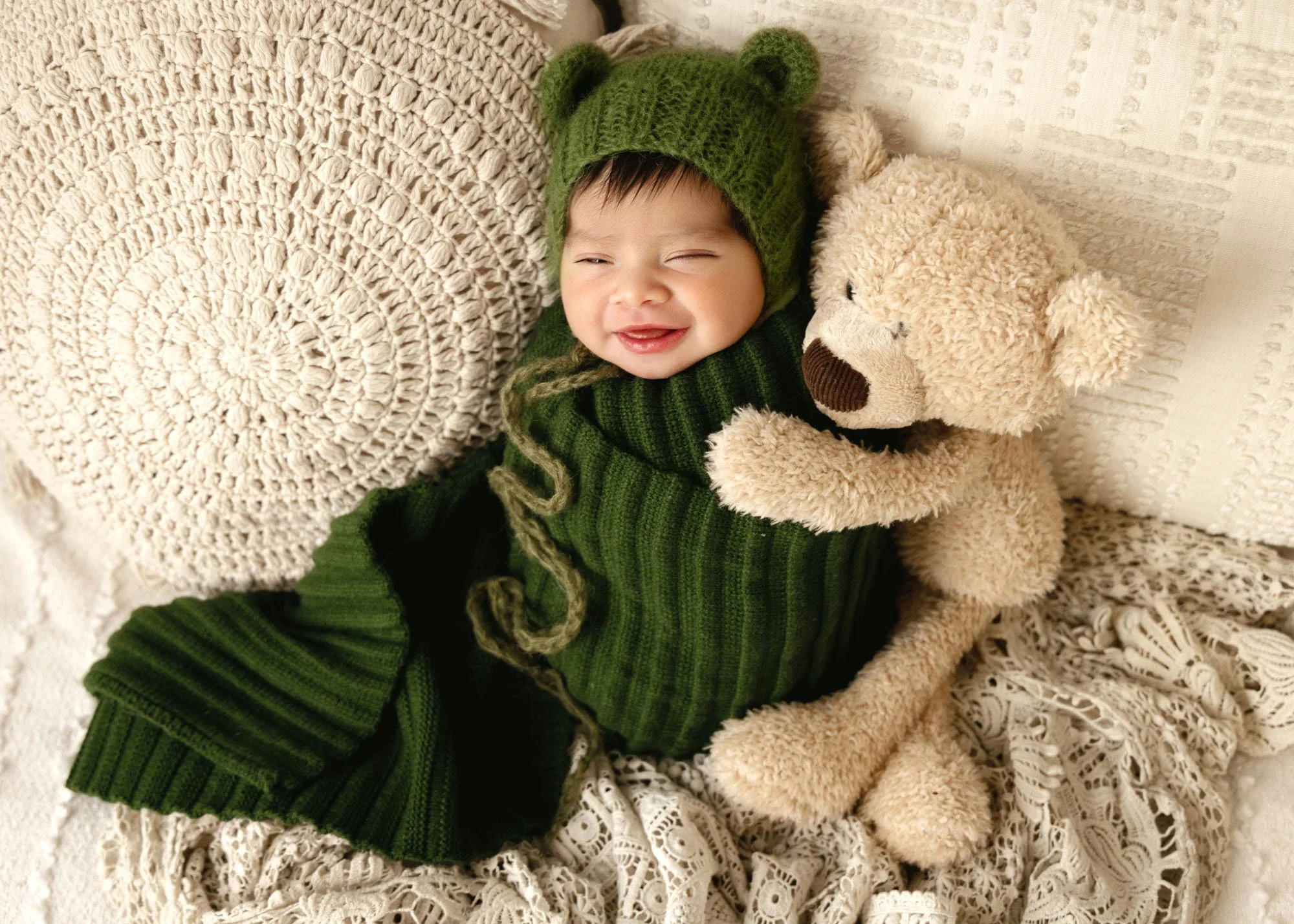 newborn baby wrapped in green with big teddy snuggling and big smile