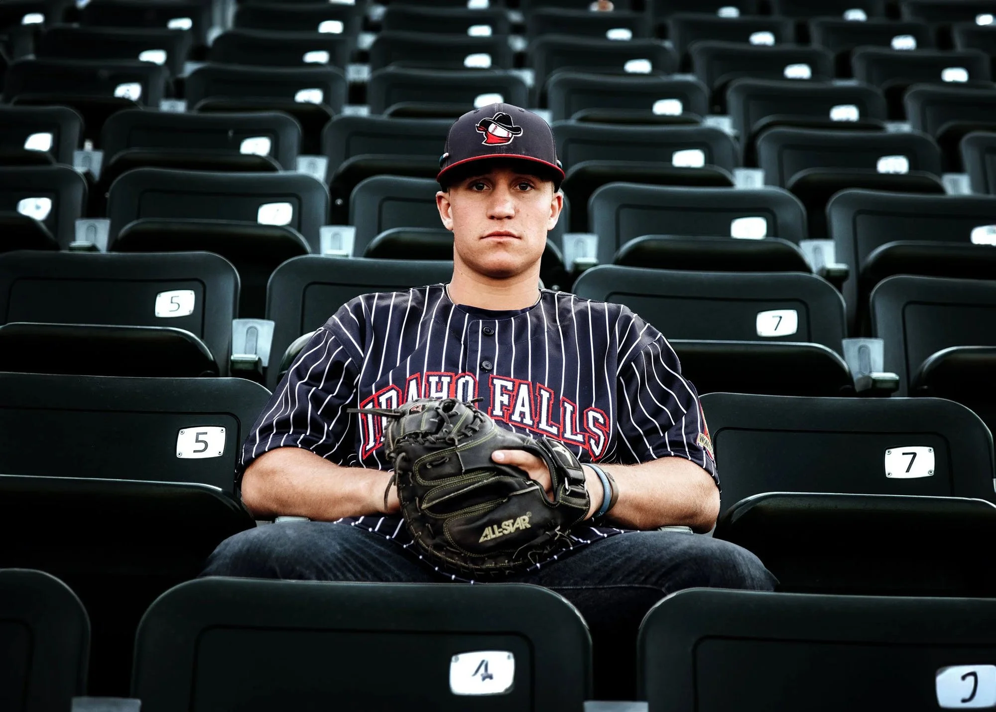 Senior boy sitting in bleacher stands with mitt and ball by himself