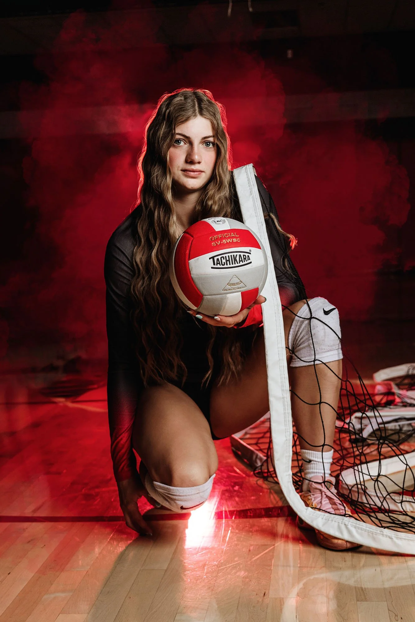 Senior girl in gym with red smoke holding volleyball in front of net