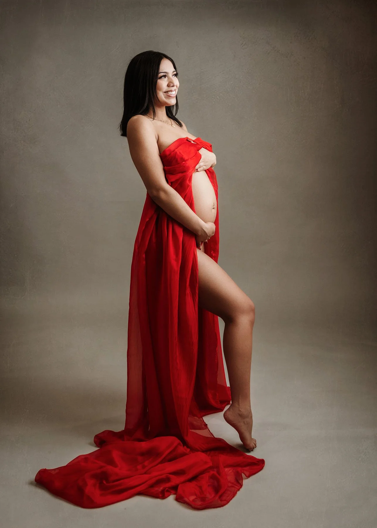 Pregnant mama in red dress holding baby bump outdoors