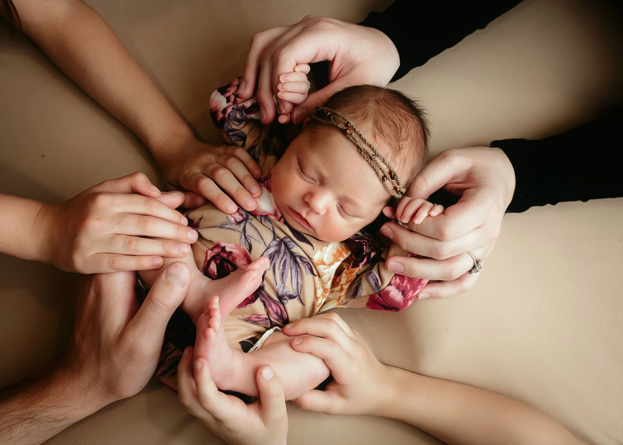 Newborn posed in miniature bed holding stuffed lamb with family hands on baby