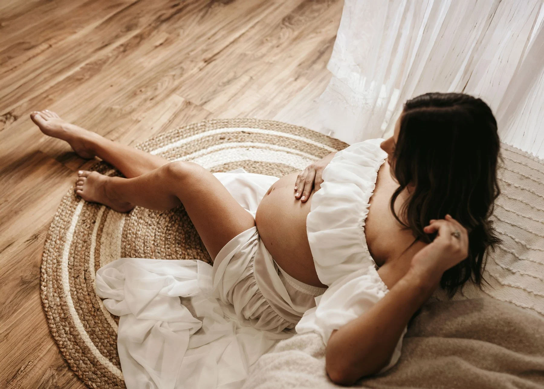 Mama sitting in front of bed in white top and skirt, baby bump showing, legs out
