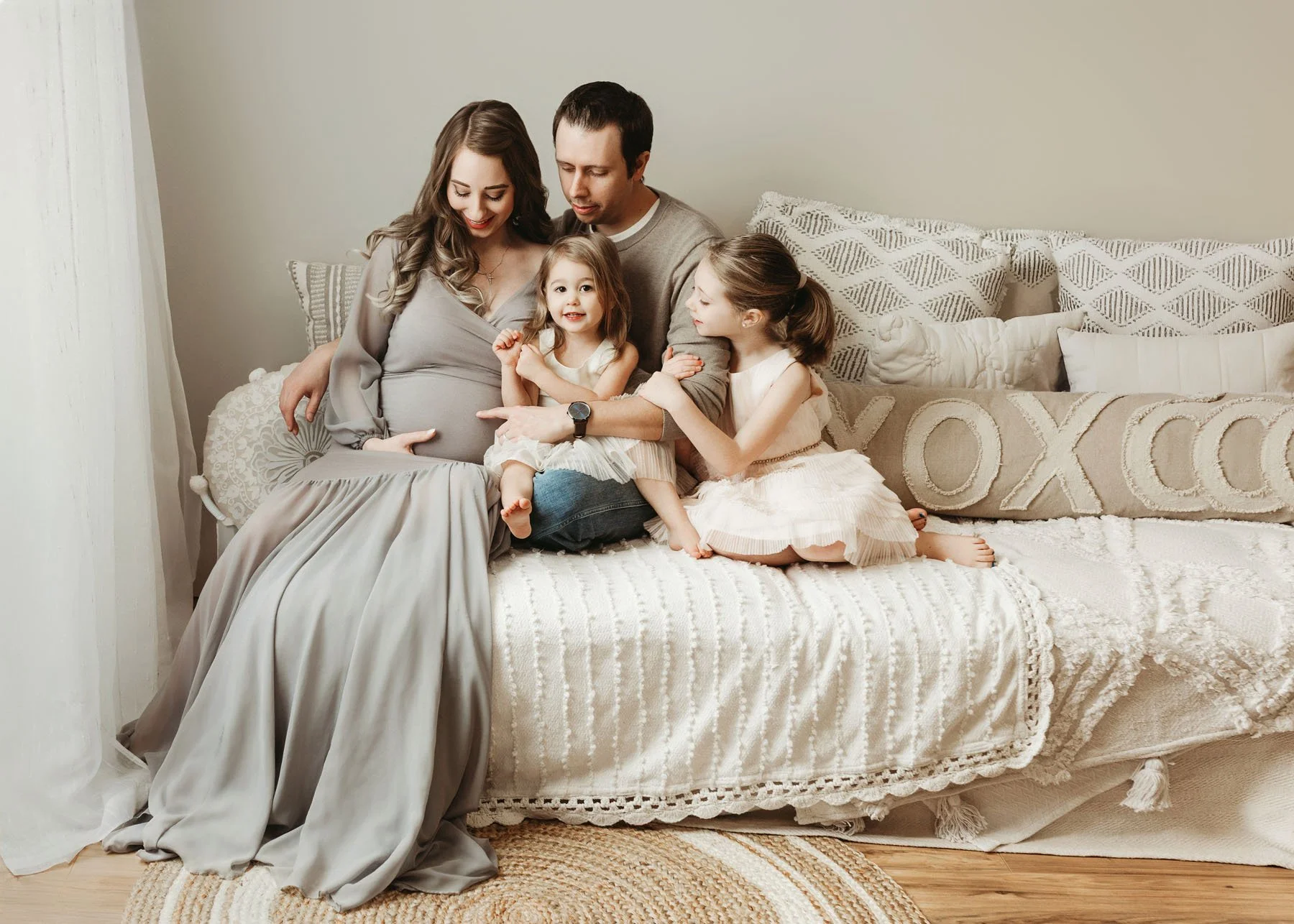 Family sitting on bed, little girl laying head on mama's baby bump