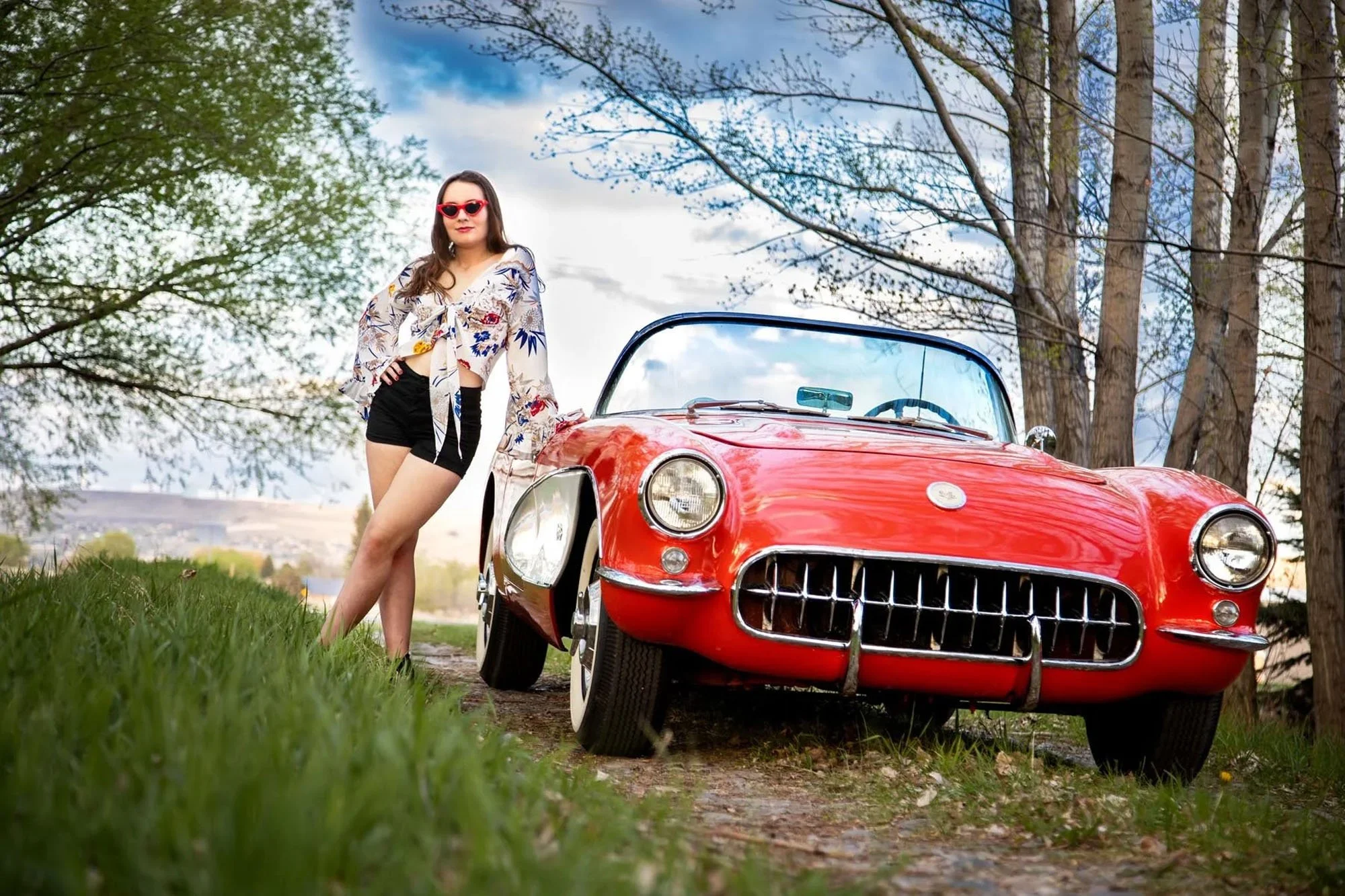 Senior girl leaning on red car with blue sky behind her