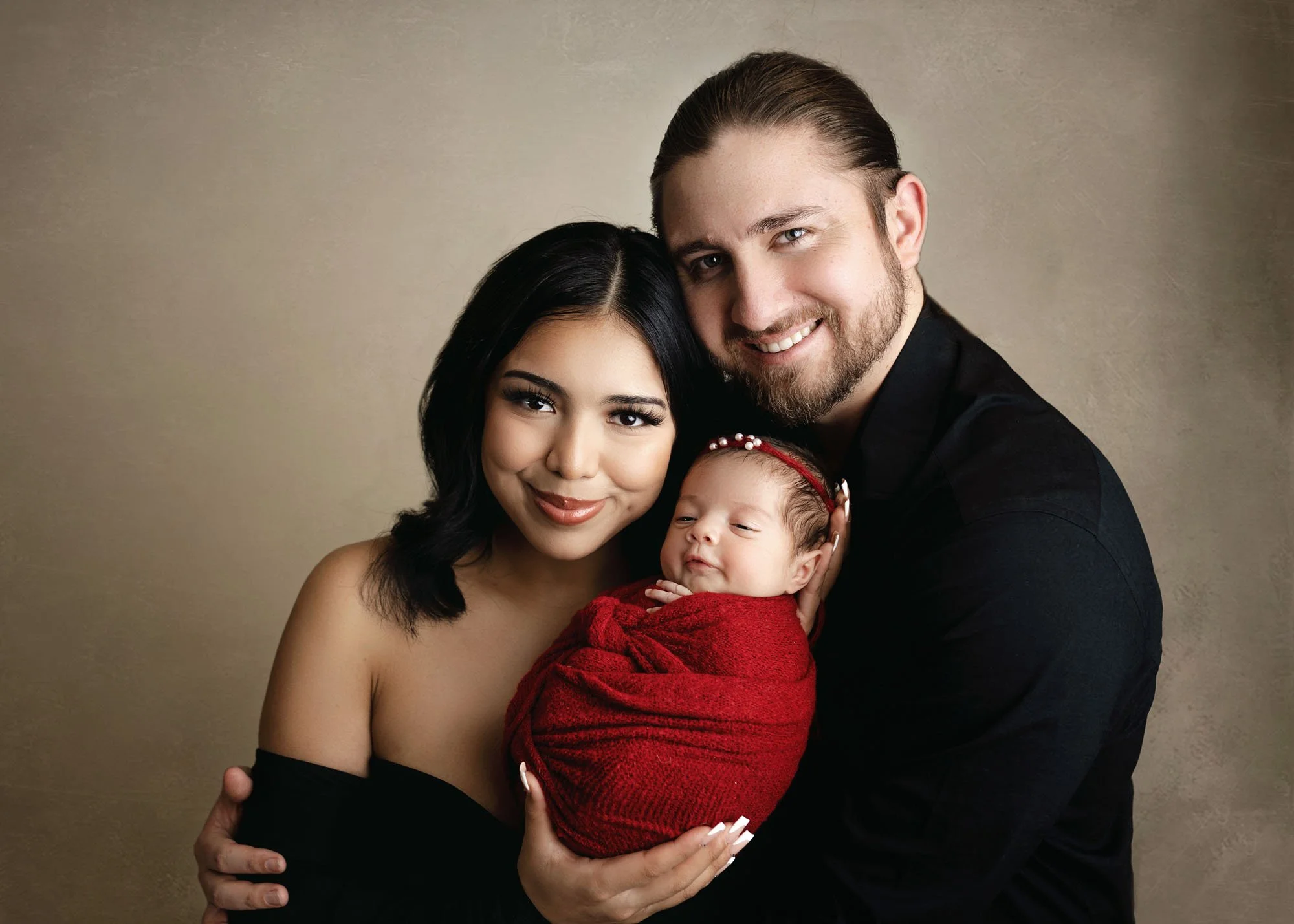 Parents holding newborn and smiling at camera during studio session
