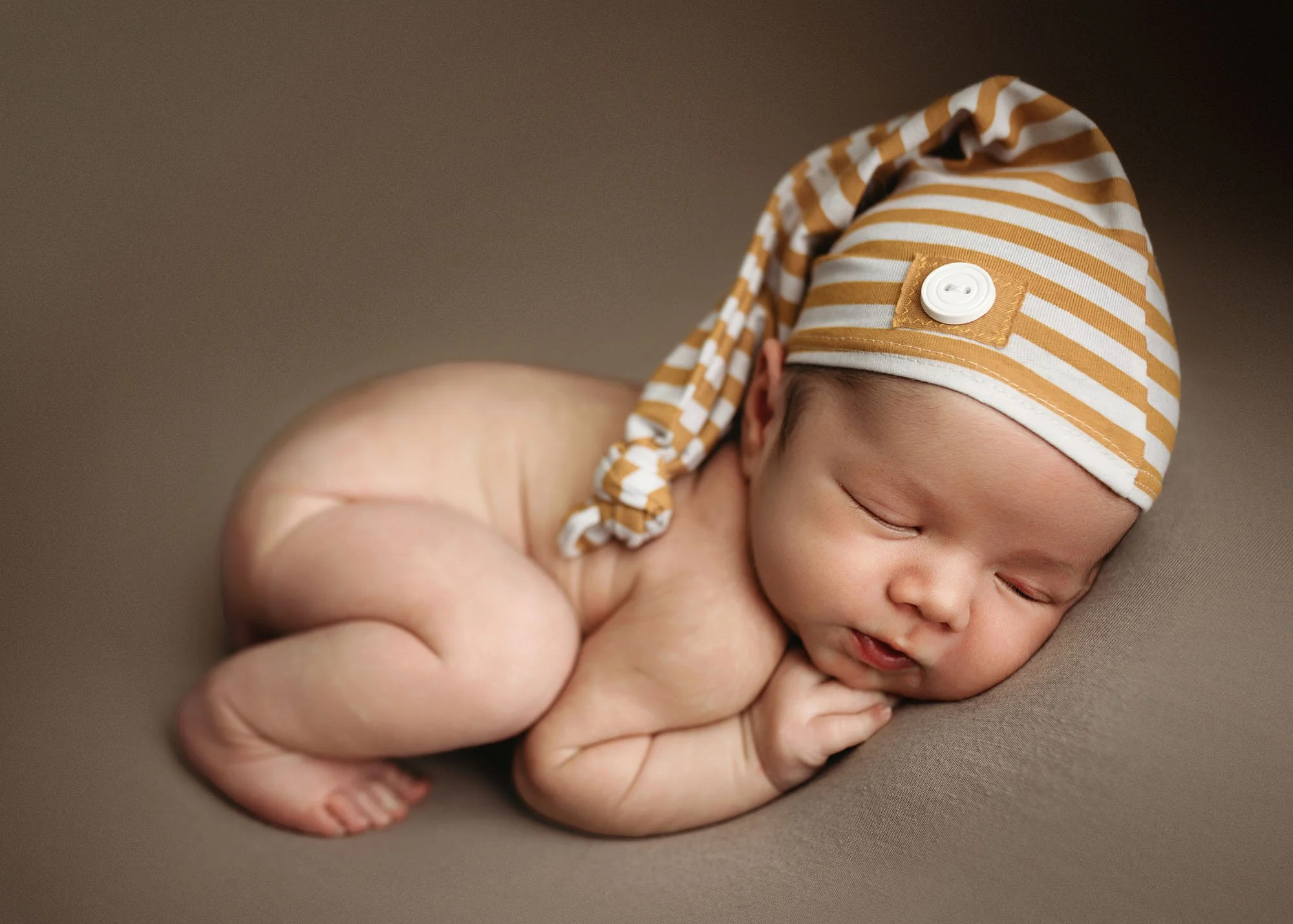 Newborn in neutral bum up pose with textured wrap and knit hat