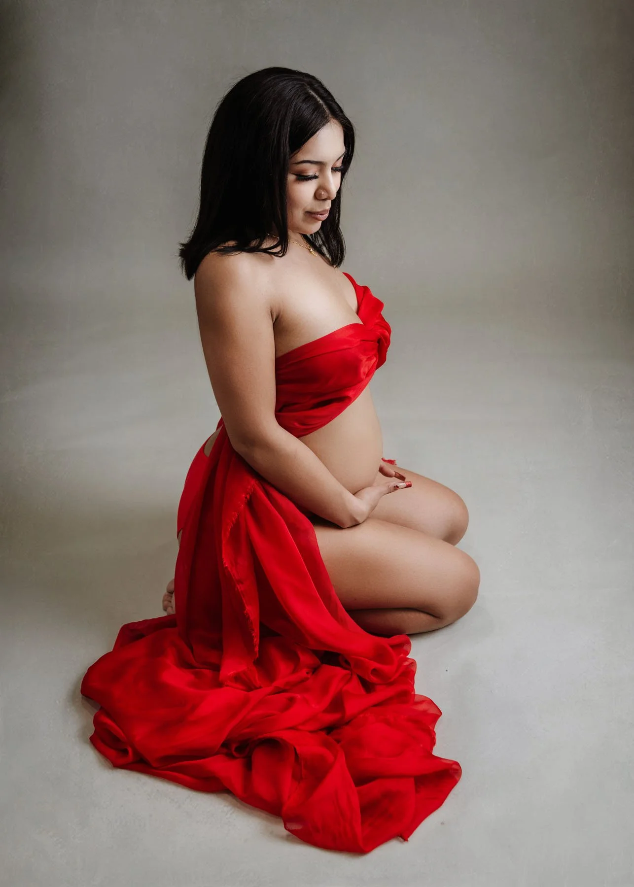 Fourth mama in red dress outdoors holding baby bump