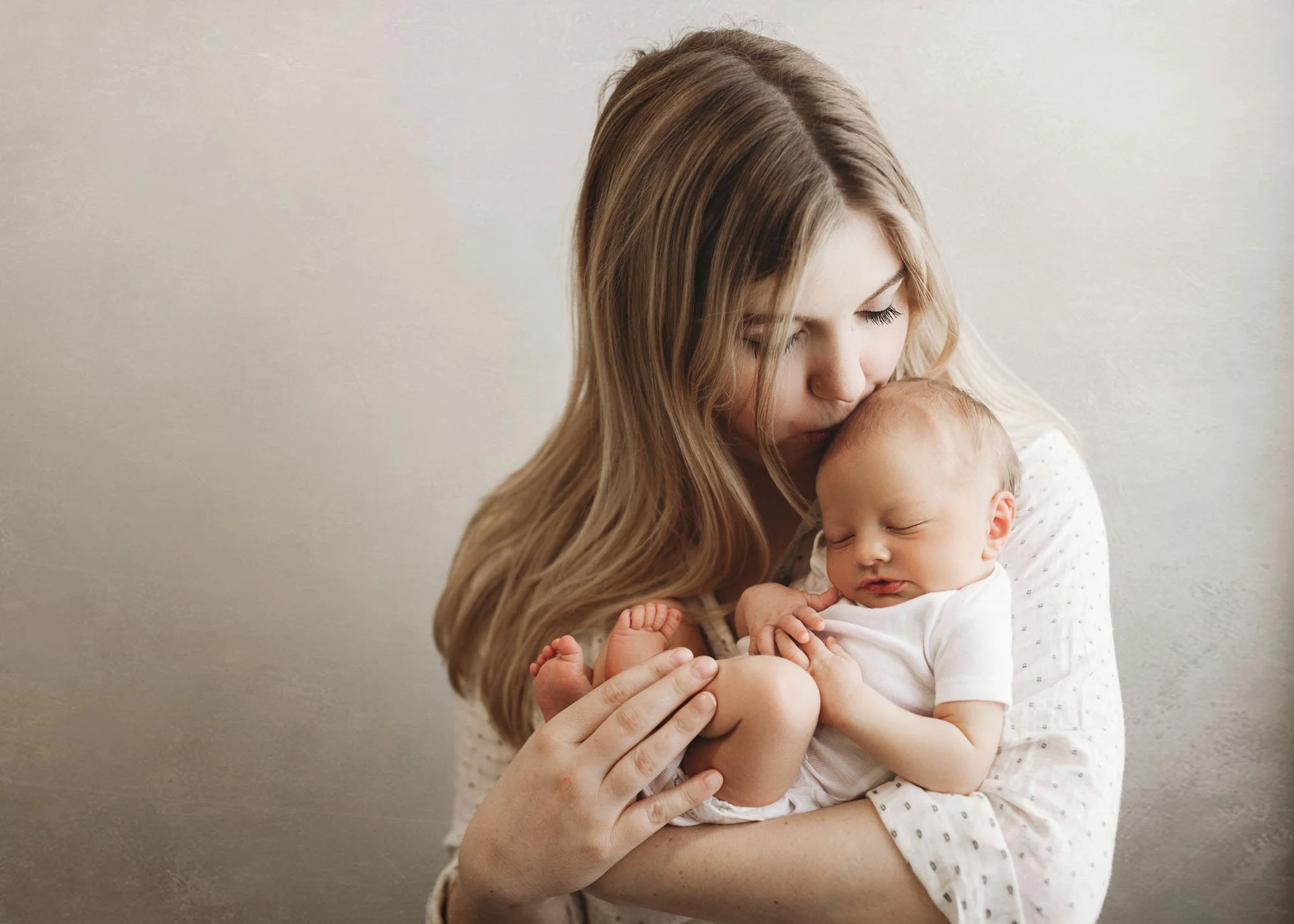 Mother holding newborn while father kisses her cheek during newborn session