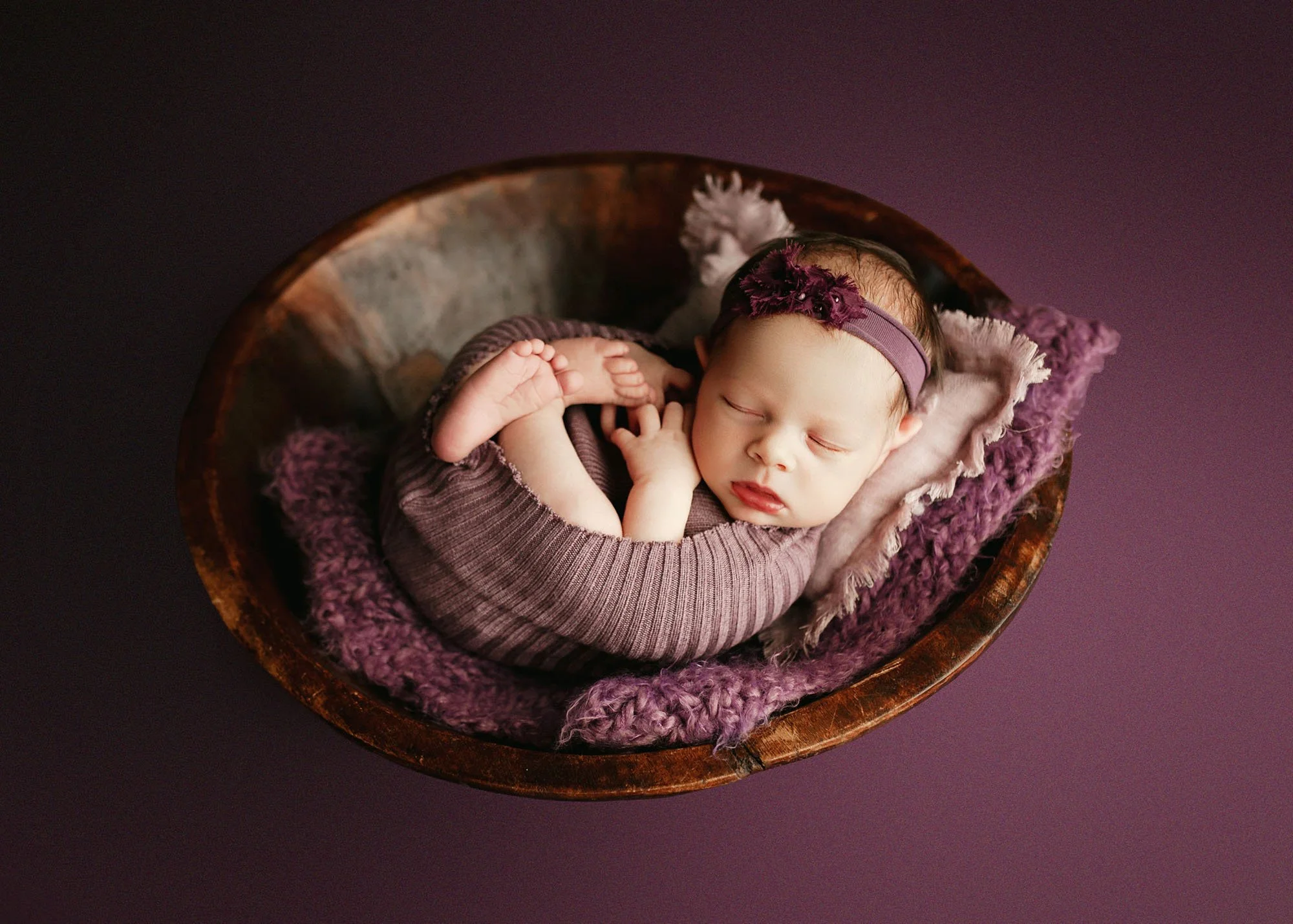 newborn in purple laying in rustic bowl