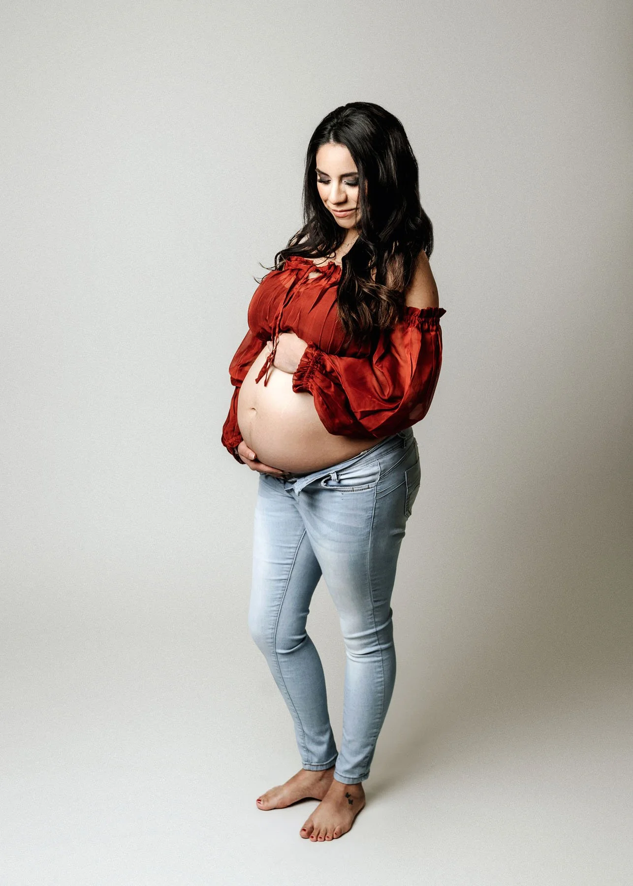 Second mama in red dress outdoors holding baby bump