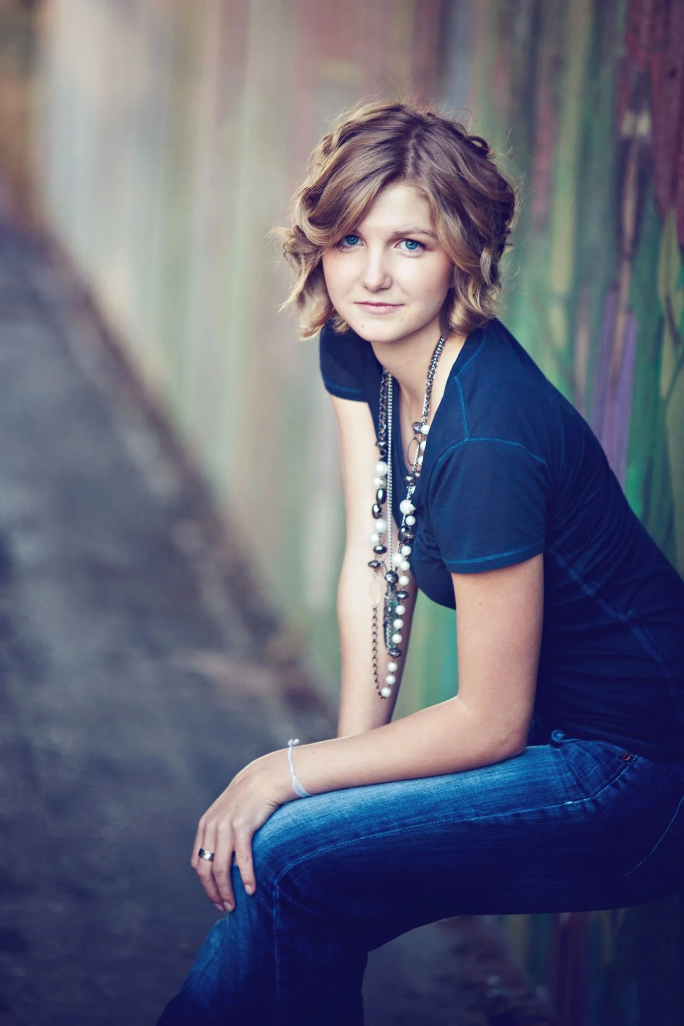 Senior girl in blue shirt leaning on wall looking at camera outdoors