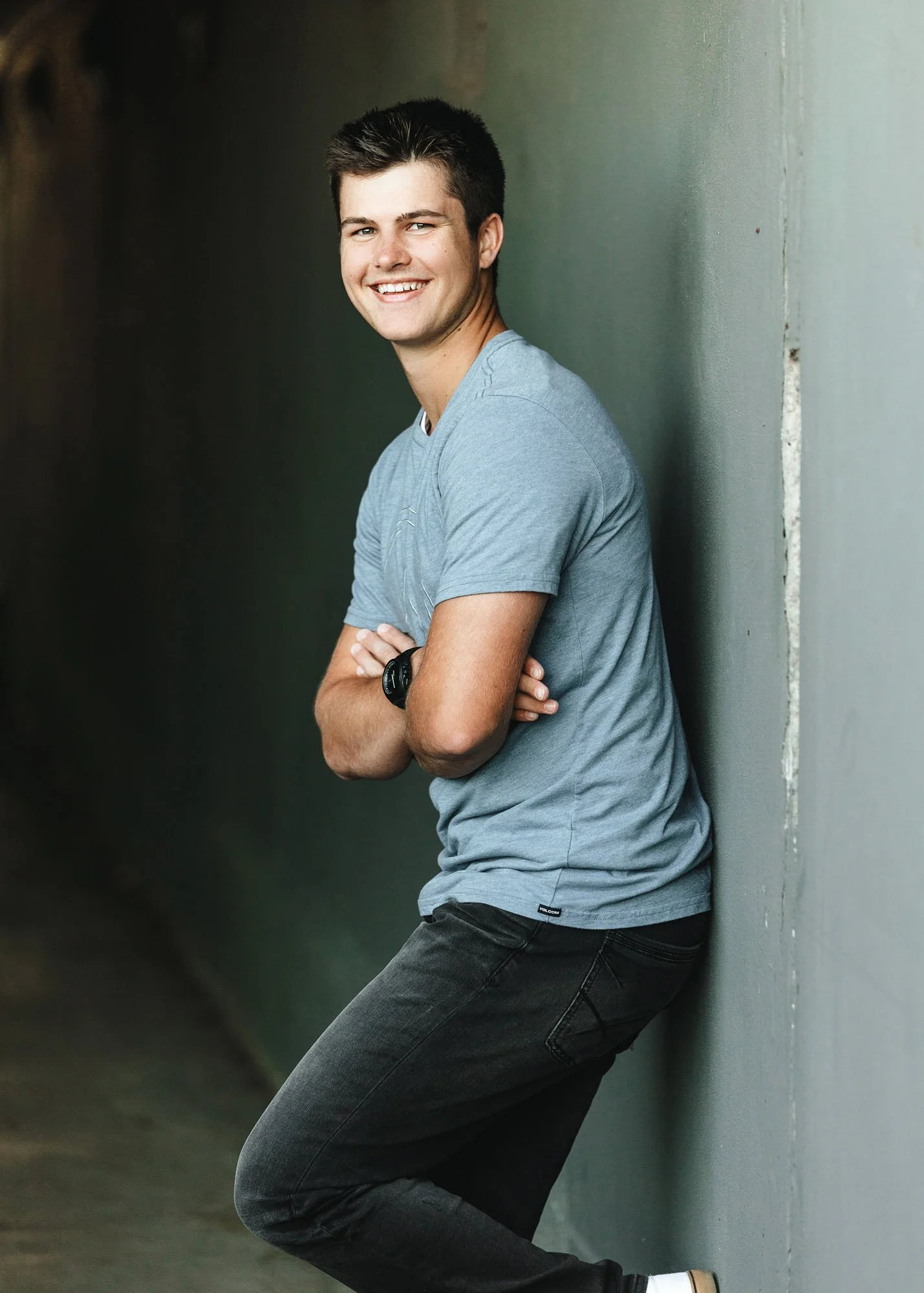 Teen boy leaning against wall wearing blue shirt in senior portrait