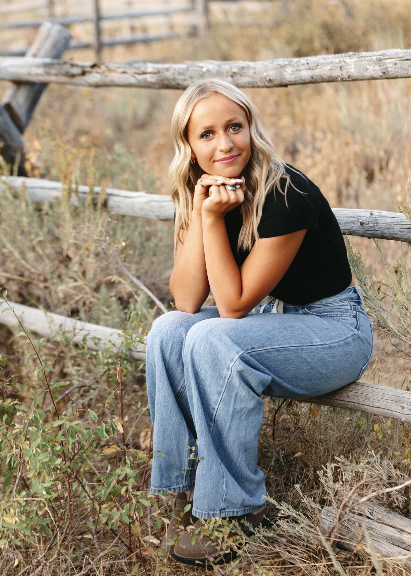 Senior girl sitting on fence with hands folded under chin