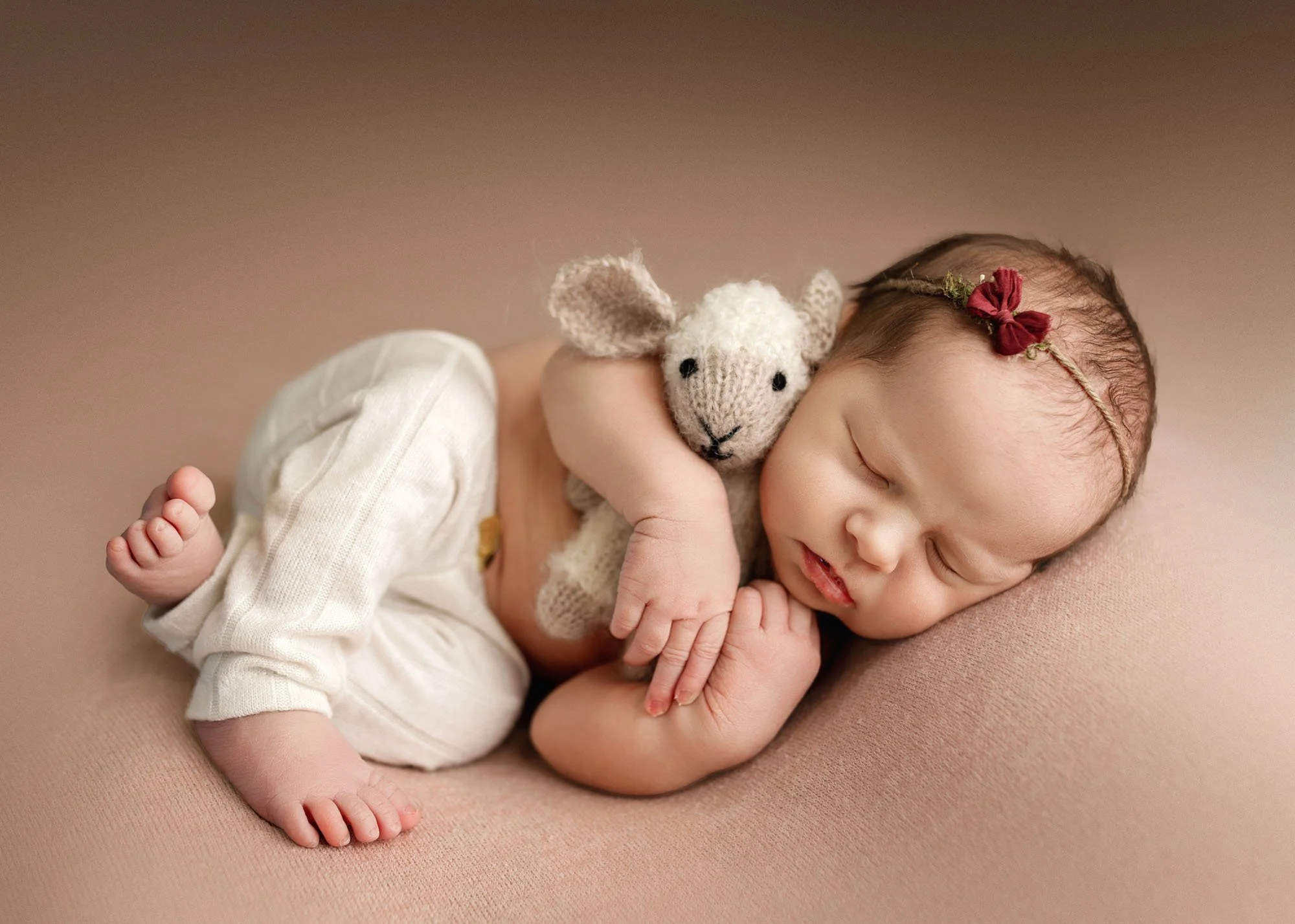 Newborn laying on side holding stuffed lamb during studio session