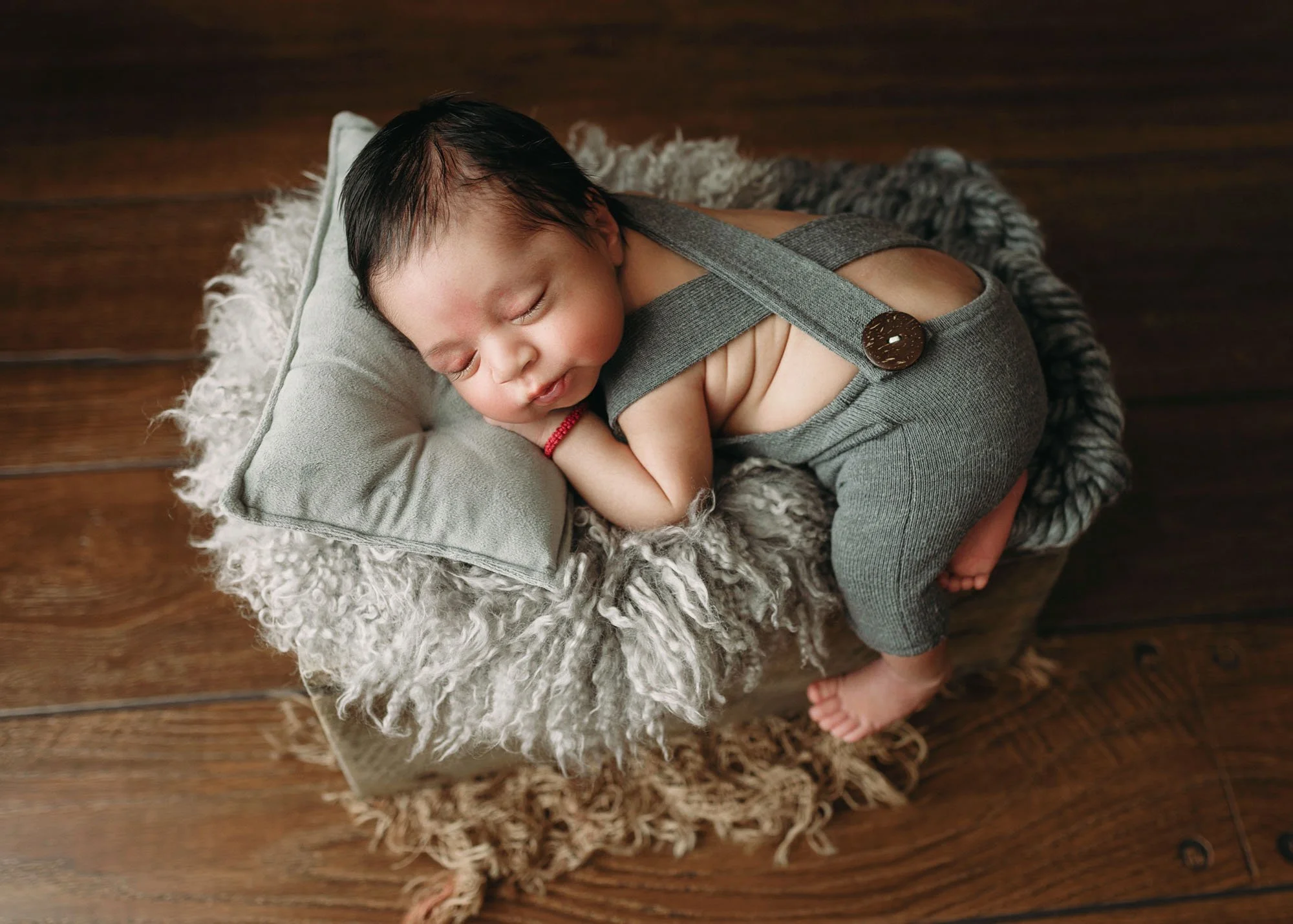 Newborn laying on tummy on miniature bed prop smiling
