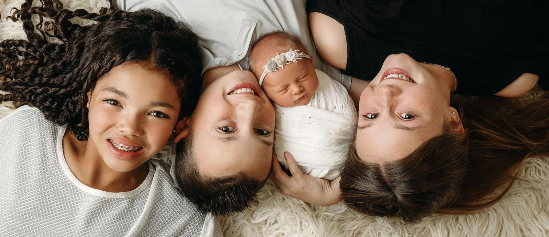 siblings laying with newborn in a row