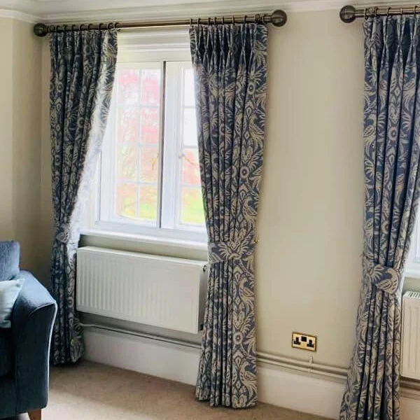 Image of two pairs of full length curtains on brass rods, the curtains have a denim blue bird pattern on a cream background.