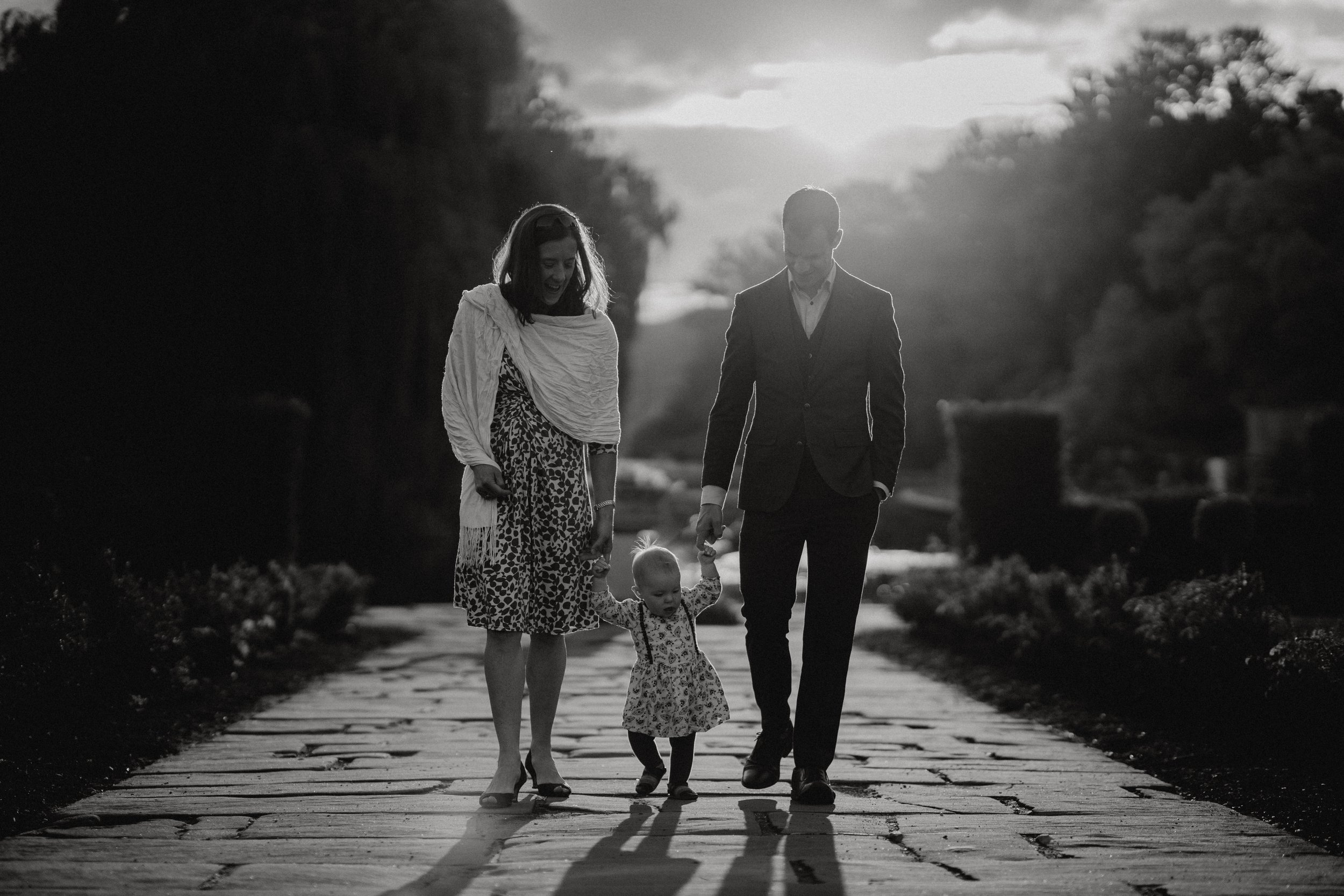 Black and white photo of a family walking down a path, with a man and woman holding hands with a toddler between them at Coombe Abbey, Coventry