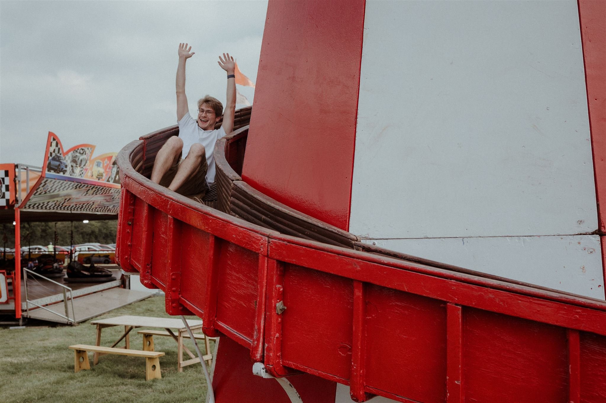 Person sliding down a red and white amusement park ride with arms raised, excited expression.