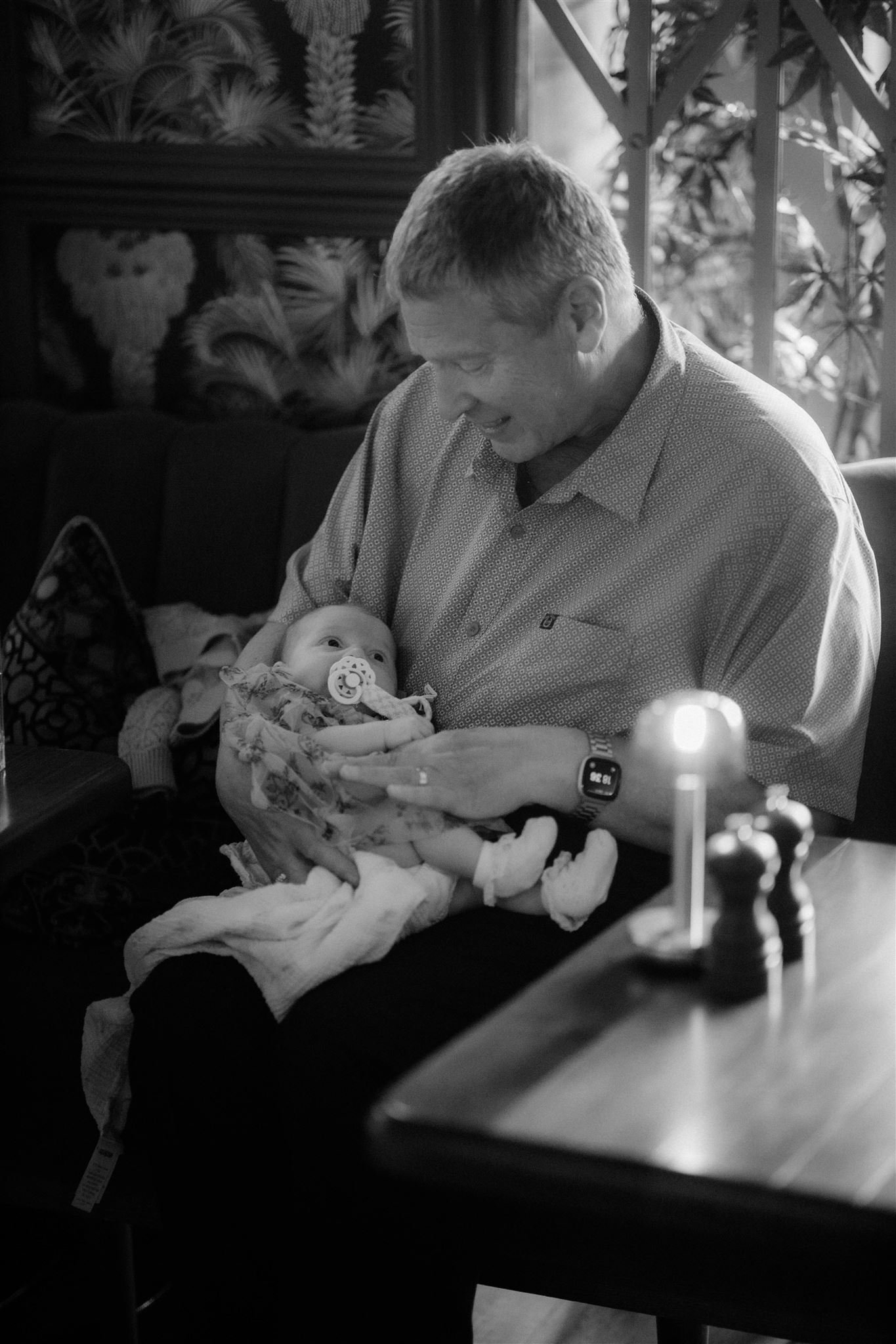 Man holding a baby with a pacifier in a dimly lit room.