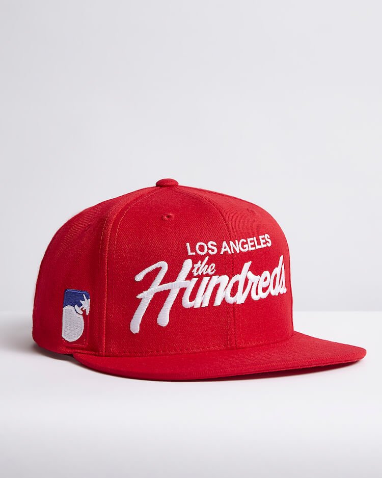Red snapback cap with white "Los Angeles the Hundreds" embroidery and bomb logo on the side.