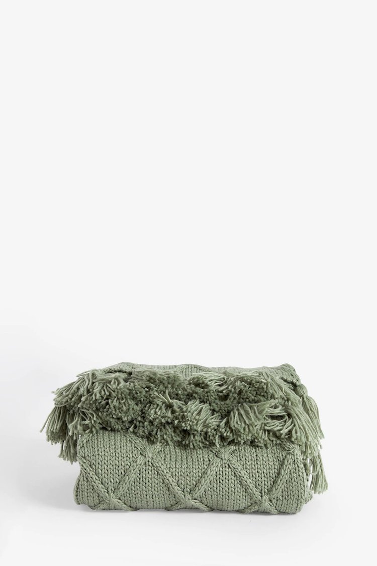 Green knitted throw blanket with fringes, folded neatly on a plain background.