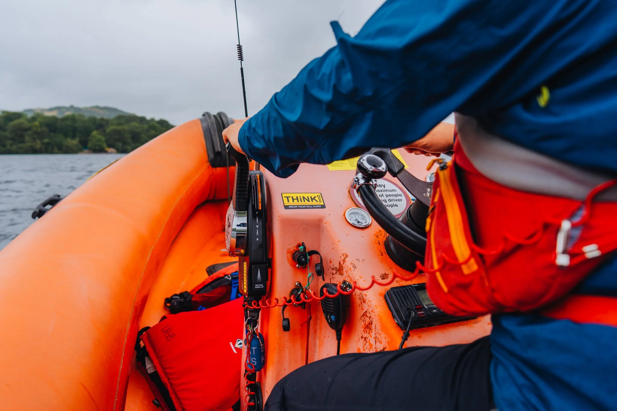 Freelance outdoor Lifestyle Photographer Close-up of a person operating an orange inflatable boat, showing the boat's dashboard with navigation and communication equipment, and a life vest inside.