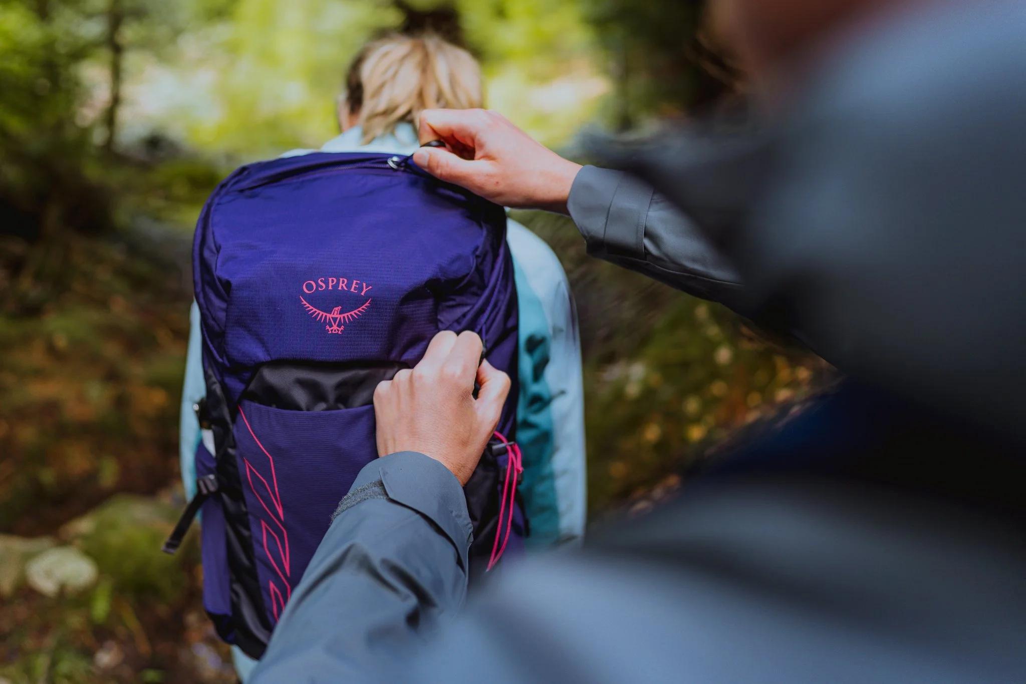 Freelance outdoor Lifestyle Photographer Person adjusting a blue Osprey backpack while on a forest trail.