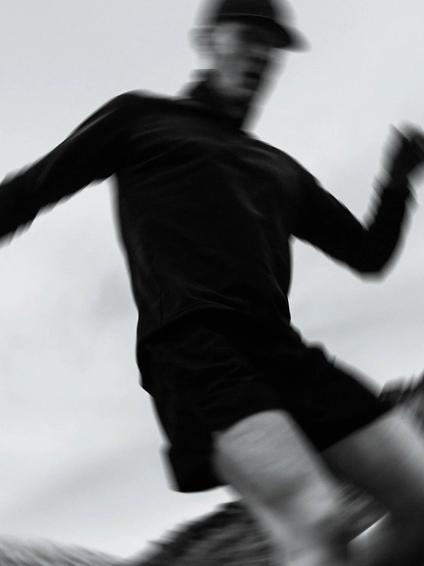 Blurred silhouette of a person running outdoors against a gray sky.