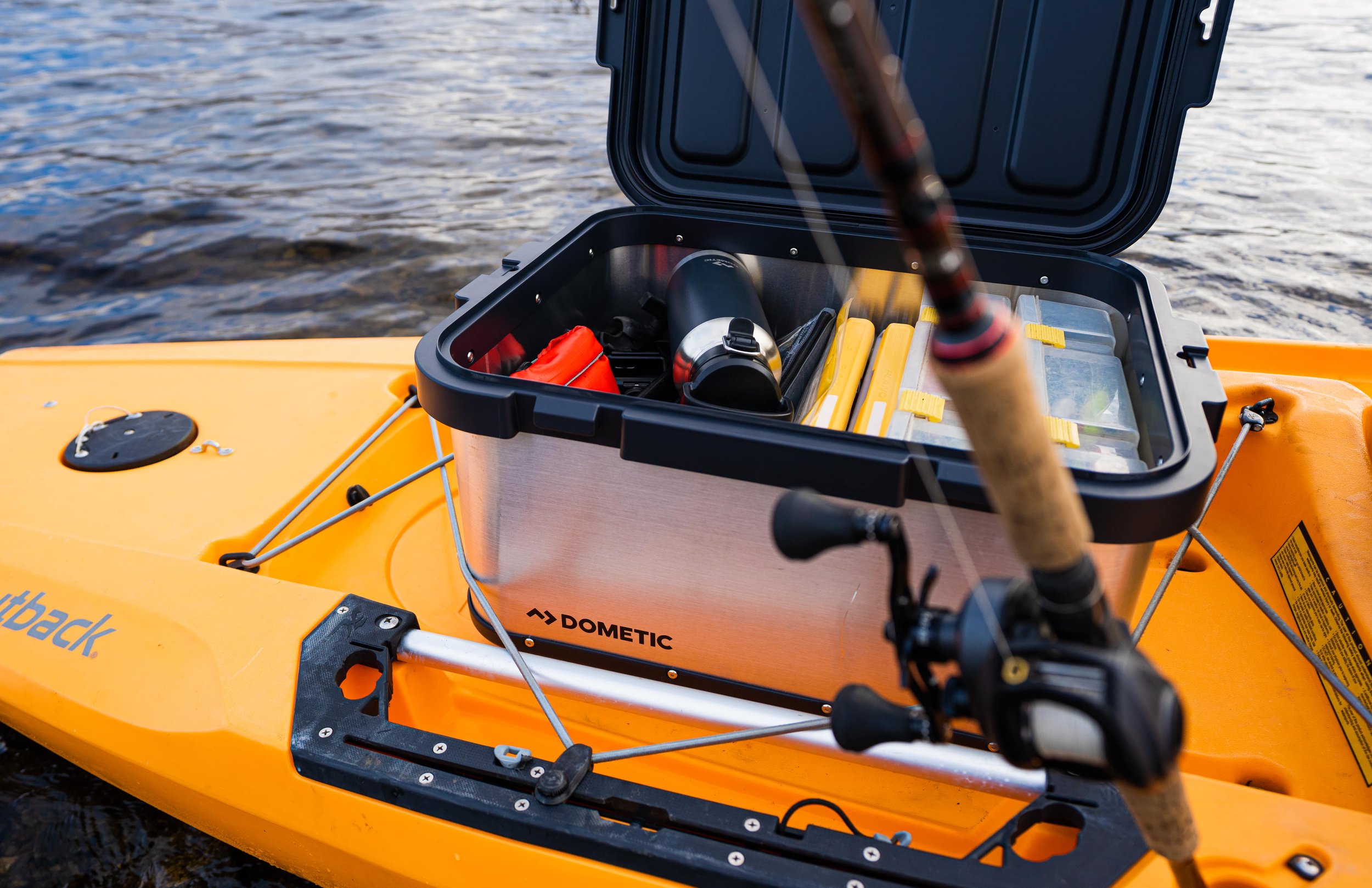Close-up of a yellow kayak with an open black storage compartment containing fishing gear and accessories, on a body of water.