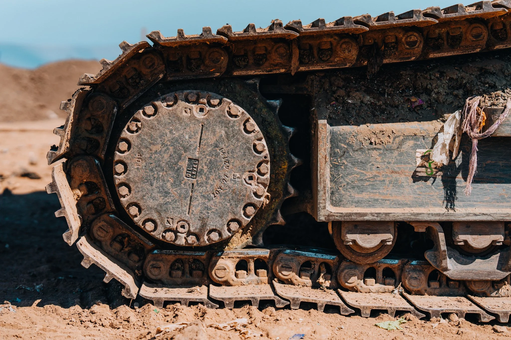 Freelance Lifestyle Photographer Close-up of a rusty tracked wheel of a construction vehicle on dirt ground, with dirt and debris around.