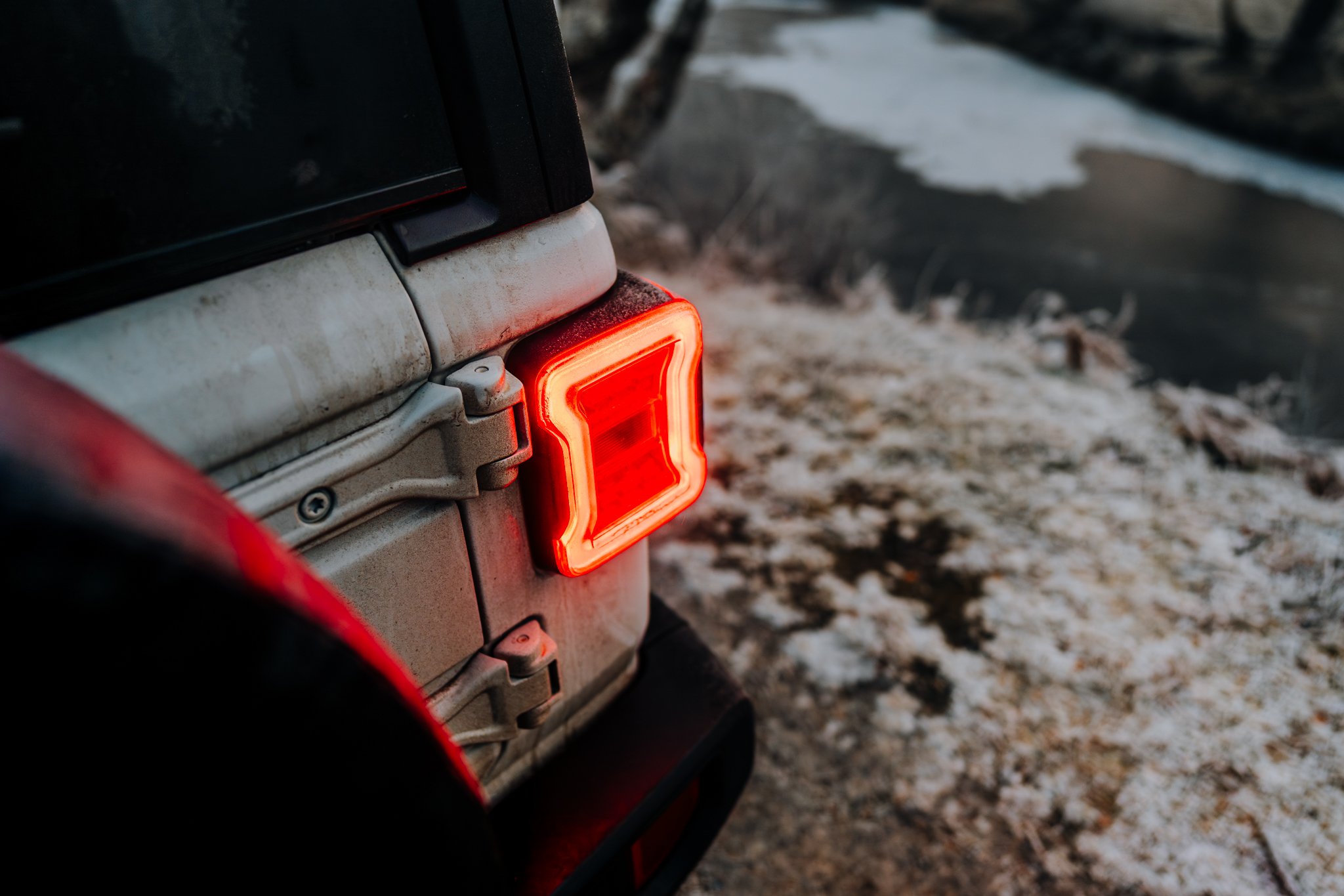 Freelance Lifestyle Photographer Close-up of the rear of a beige off-road vehicle showing a glowing red tail light and snow-covered ground in the background.