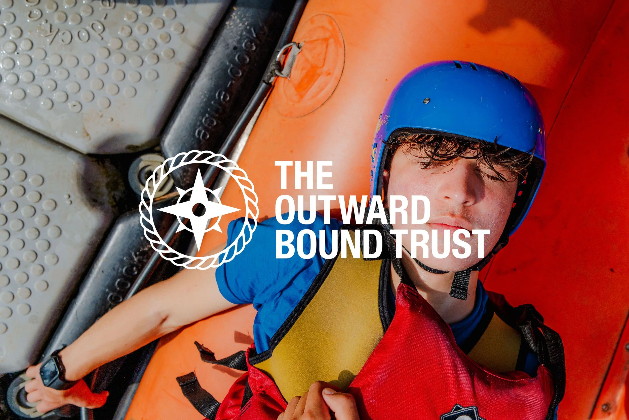 Freelance Lifestyle Photographer A young male wearing a blue helmet and a life jacket, lying on an orange kayak, with his eyes closed.