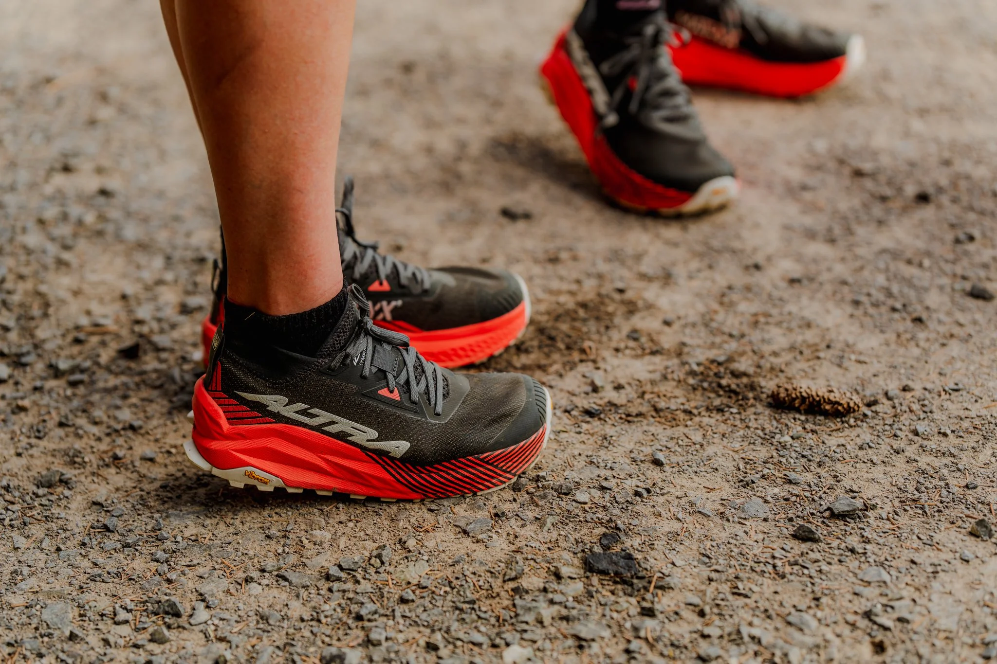 Close-up of a person's feet in black and red trail running shoes standing on a dirt trail.
