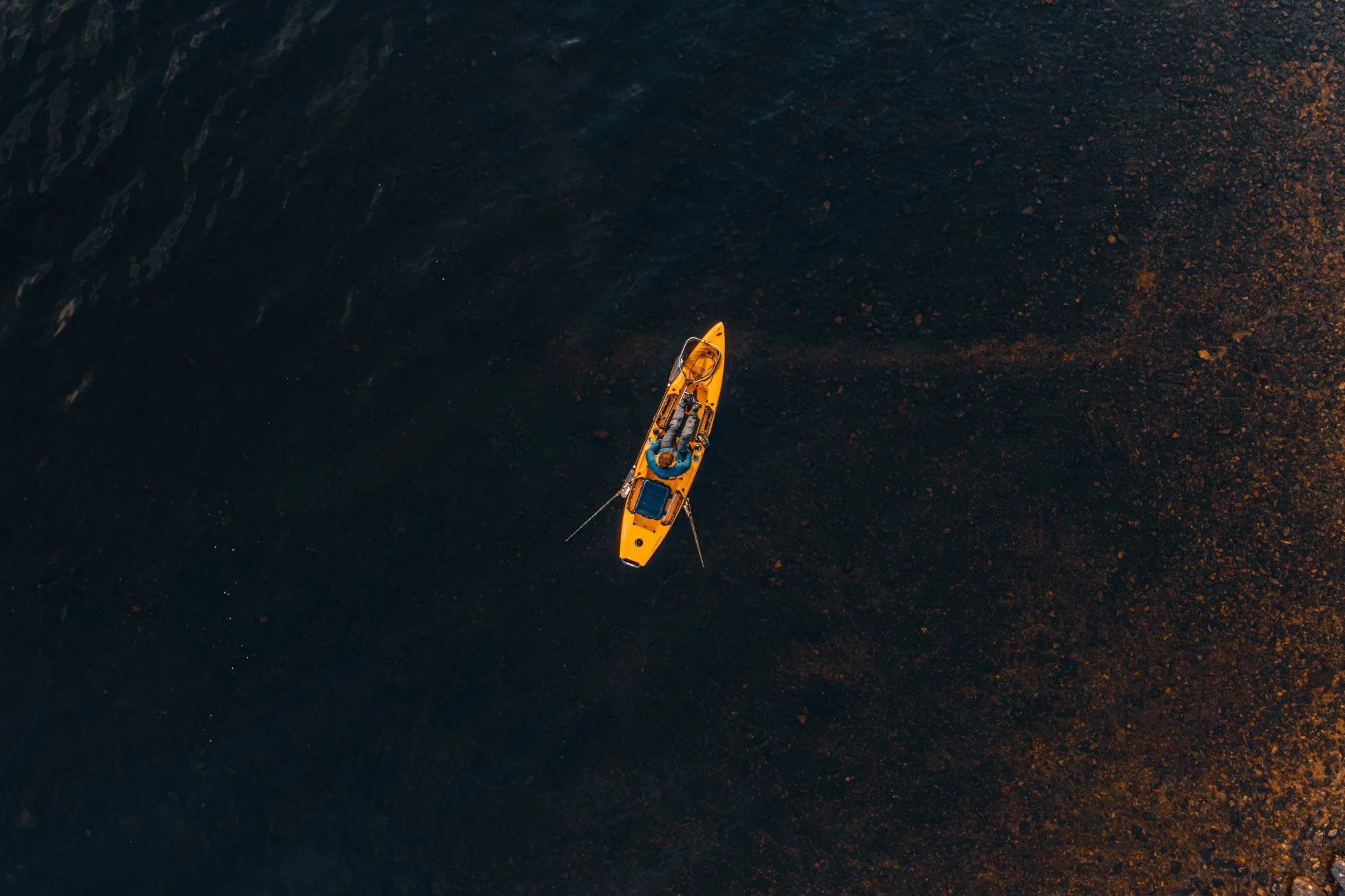 Freelance outdoor Lifestyle Photographer A person kayaking on dark water at sunset or sunrise, with an orange kayak and a paddle.