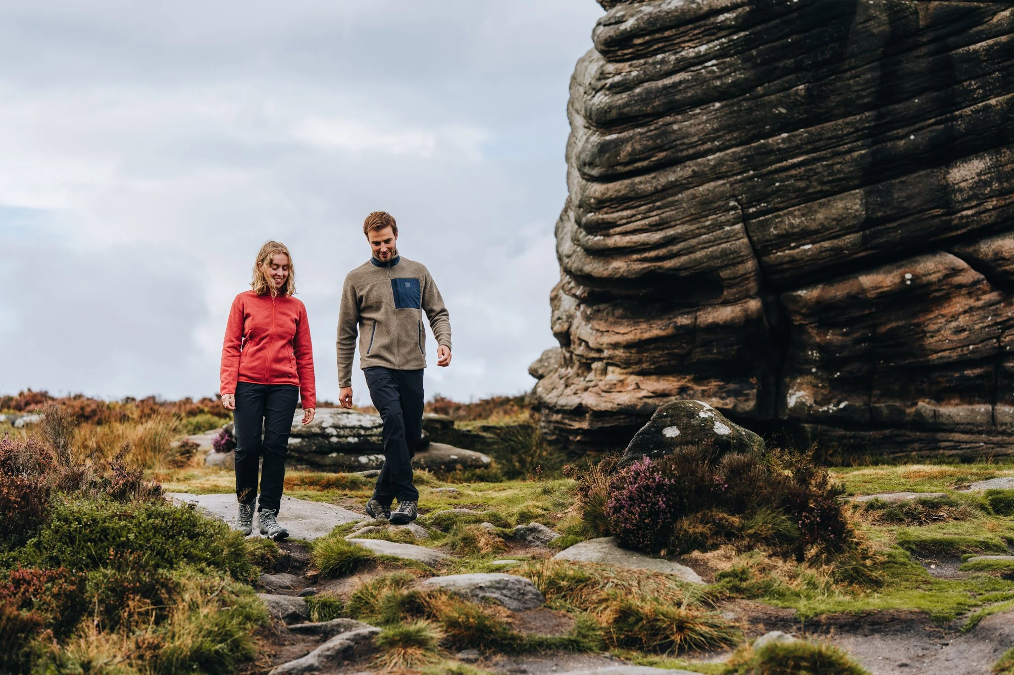 Freelance outdoor Lifestyle PhotographerA man and woman hiking on a rocky trail in a natural landscape with large rock formations and grass.