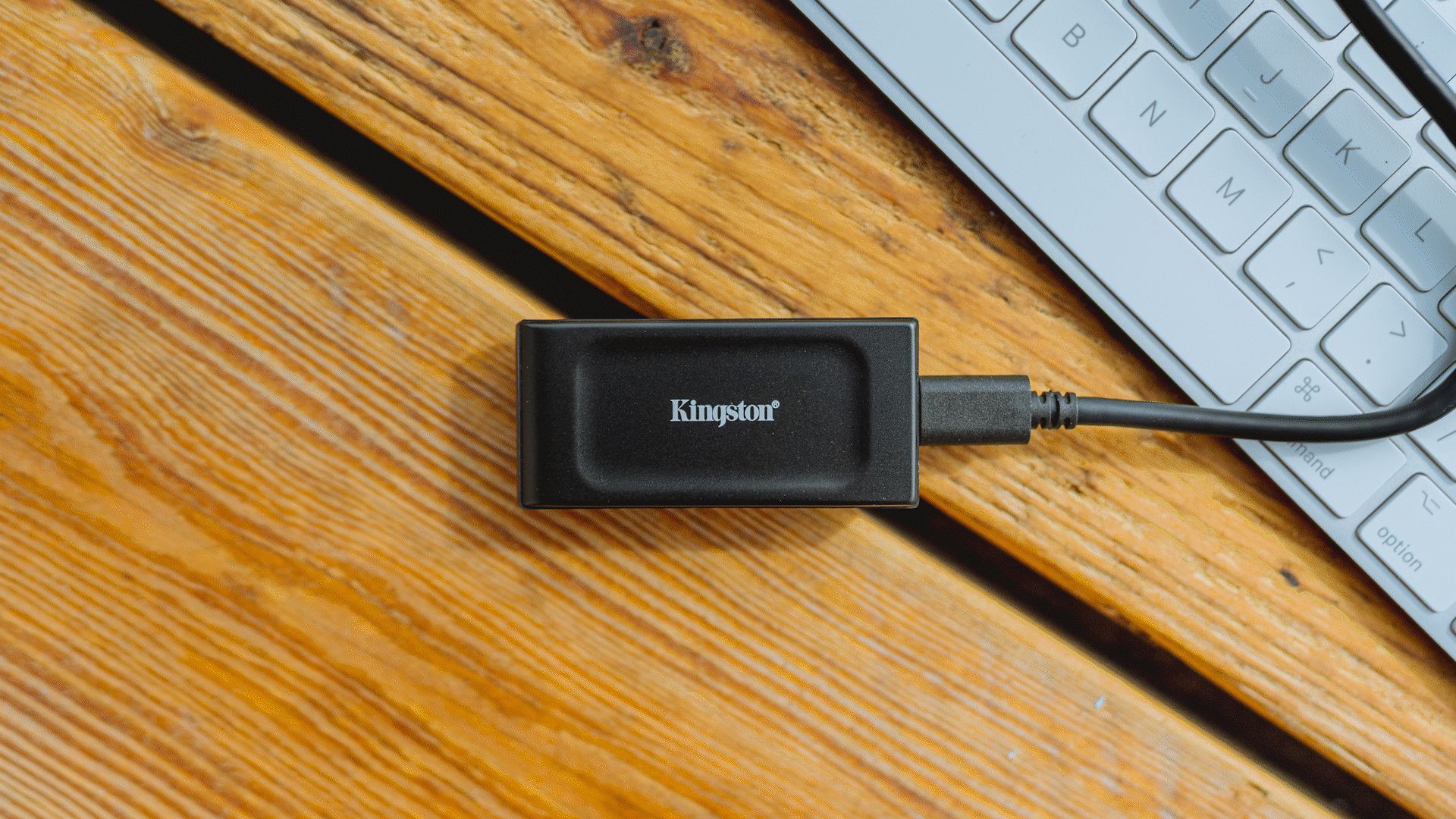 Close-up of a Kingston external hard drive connected to a laptop with a wooden desk surface visible.