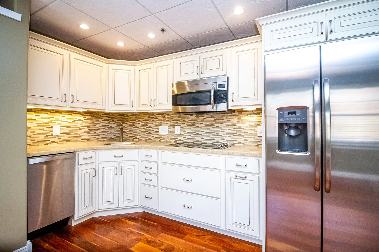 Kitchen with white cabinets, stainless steel refrigerator, microwave, and dishwasher, granite countertop, and a mosaic tile backsplash.