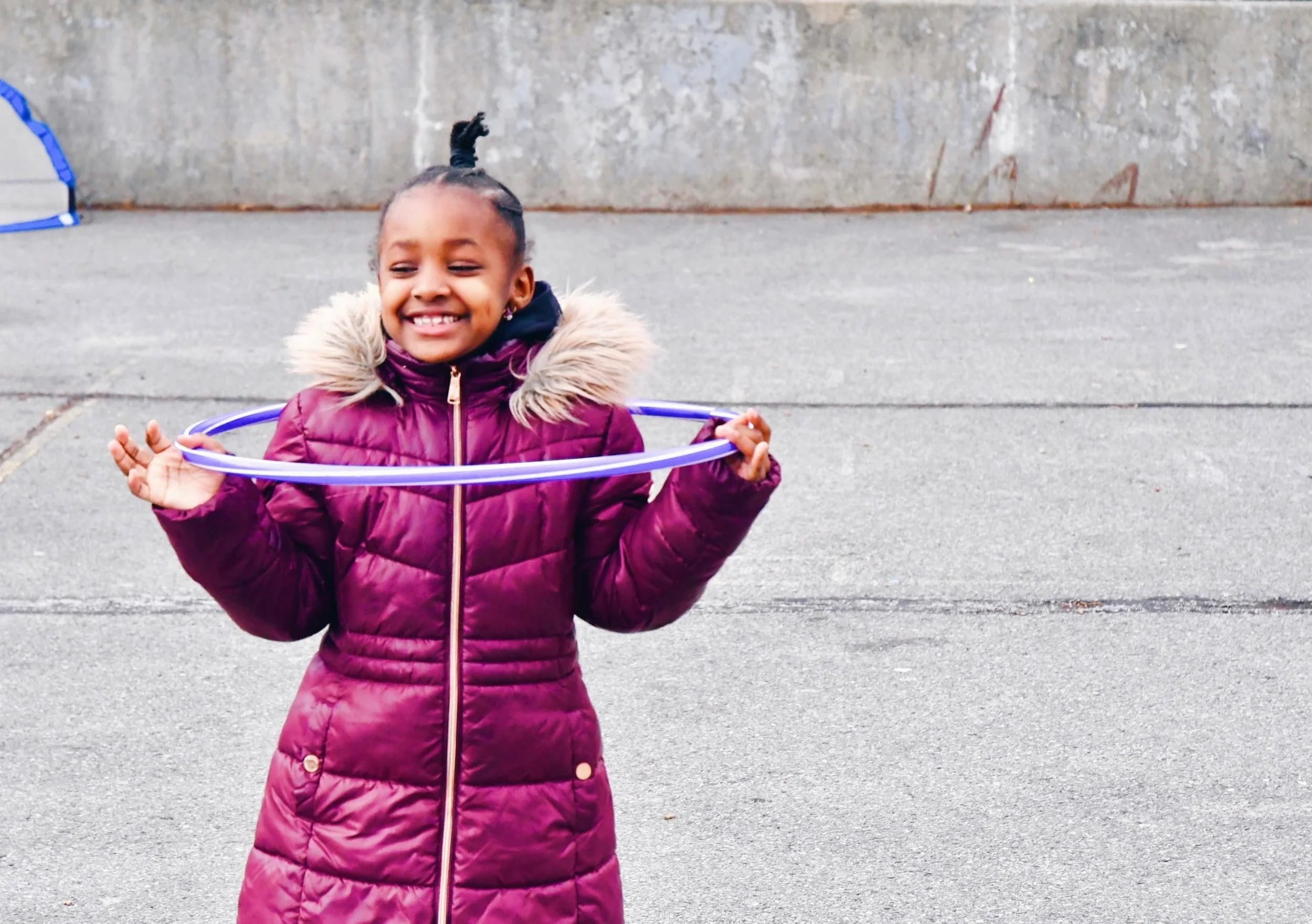 Young african american girl in a pink coat playing with a hula hoop