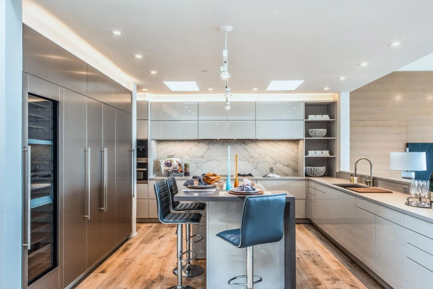 Modern kitchen with island, bar stools, marble backsplash, wood flooring, and sleek cabinetry.