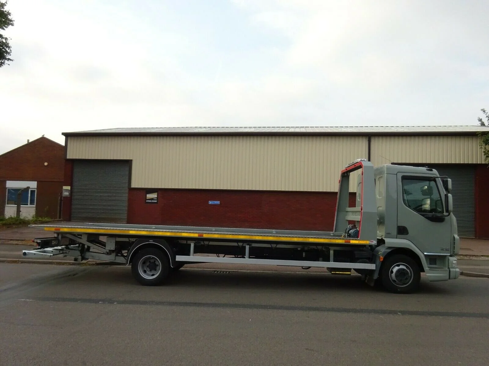 Flatbed truck parked on a street in front of an industrial building.