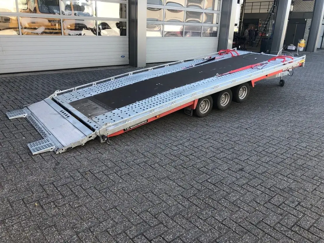 Flatbed car trailer with three axles on a paved surface