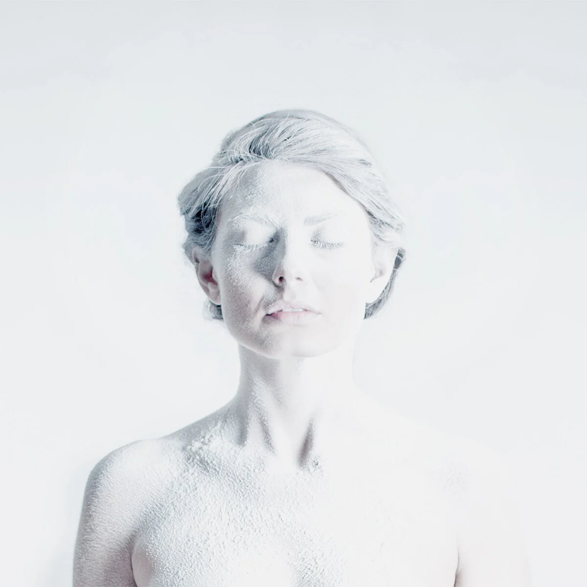 Conceptual portrait photograph by artist Ava Bock featuring a woman in an all-white room, partially obscured by white flour and fading into a blown-out white background