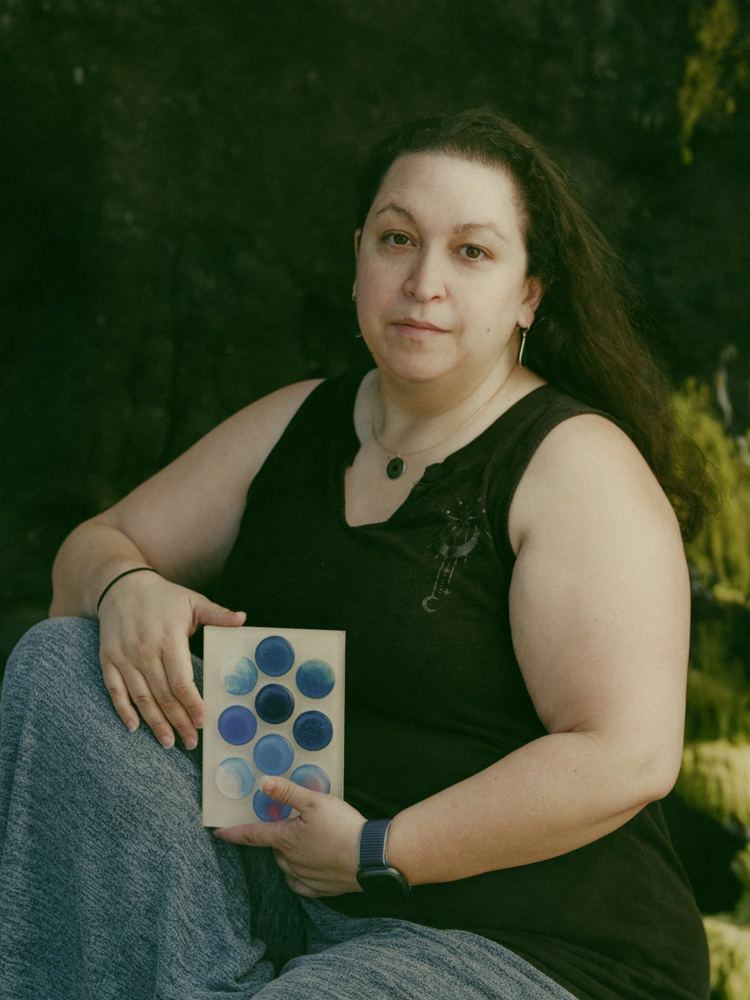 image of artist Ava Bock holding artwork in front of natural rock beach environment