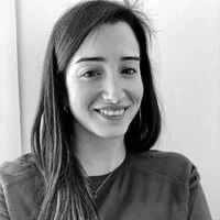 A black and white photo of a smiling woman with long dark hair, wearing a dark top.