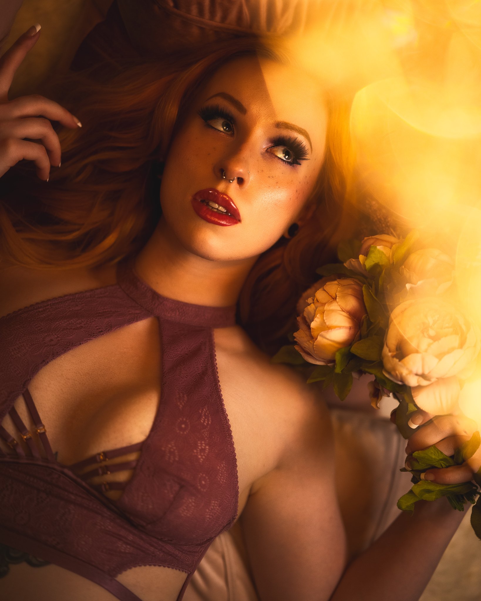 a sexy boudoir photo of redheaded model laying on a bed thinking with flowers by photographer yohance bailey based in binghamton new york  serving ithaca syracuse upstate new york.jpg
