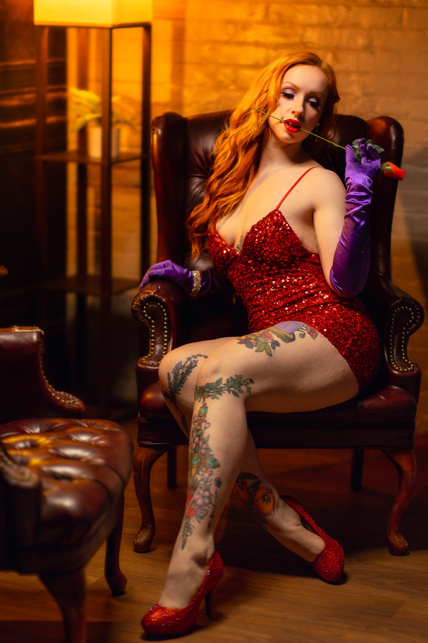 a glamour glamour photo of jessica rabbit with a rose in her mouth sitting in a a chair with tattoos by photographer yohance bailey based in binghamton new york  serving ithaca syracuse upstate new york.jpg