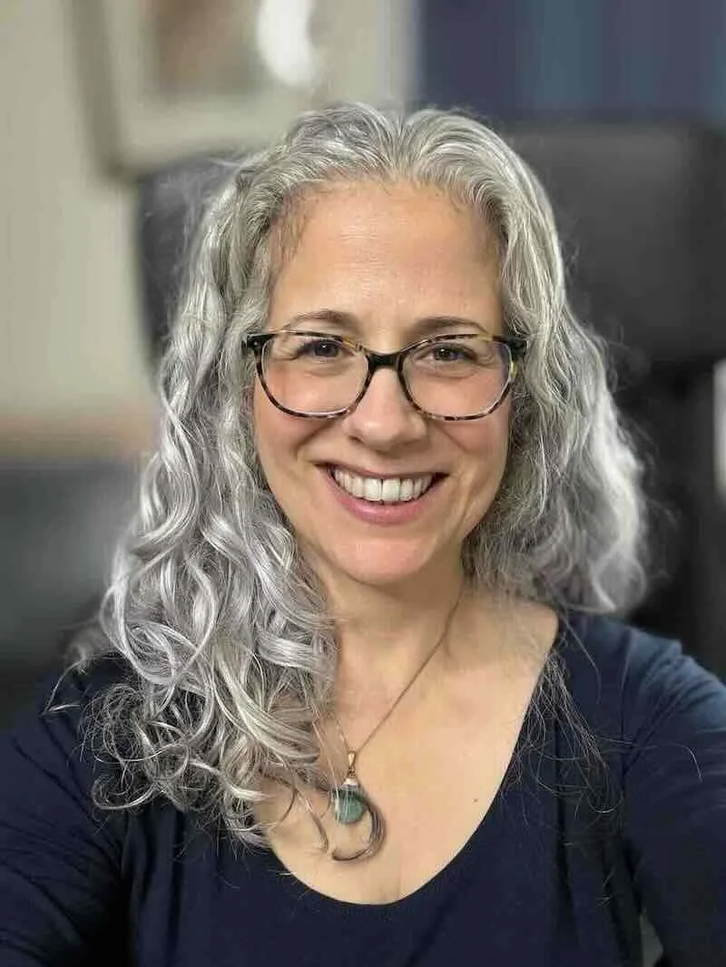 Carol Covelli, LCSW, smiling, with long gray wavy hair and dark-rimmed glasses.