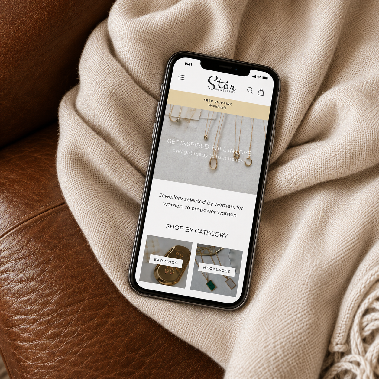 Stór Jewellery mobile homepage displayed on a smartphone on a cream blanket and brown leather sofa