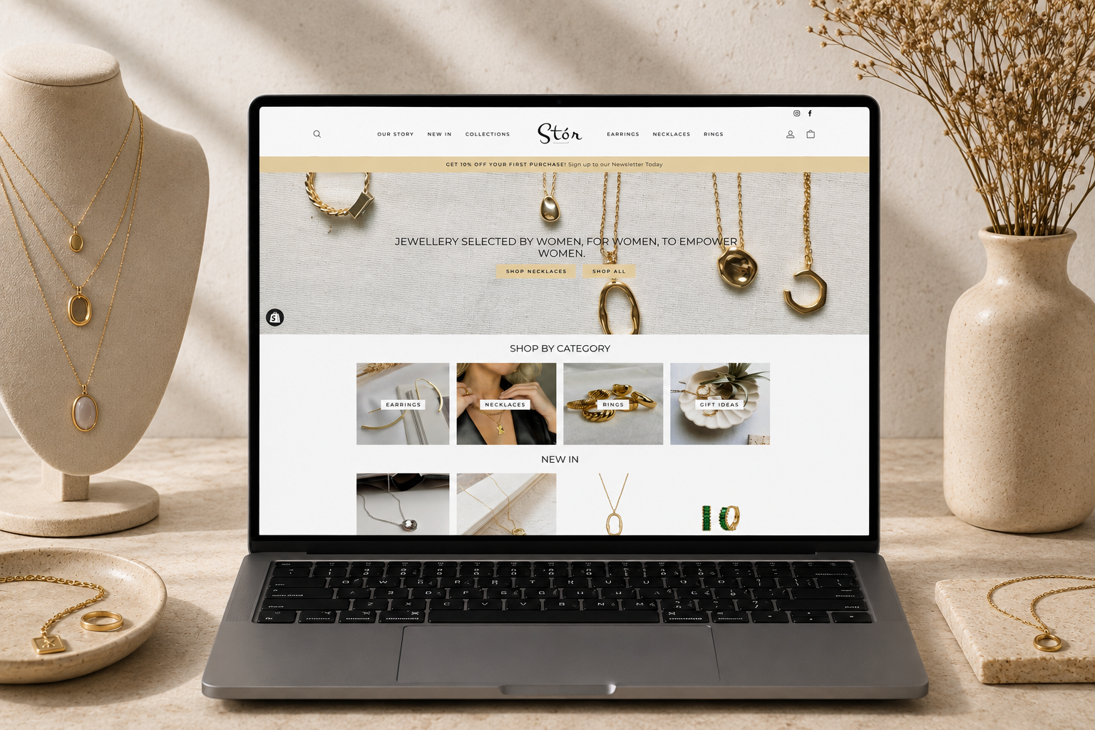 Stór Jewellery Shopify website displayed on a laptop alongside gold jewellery and a necklace stand